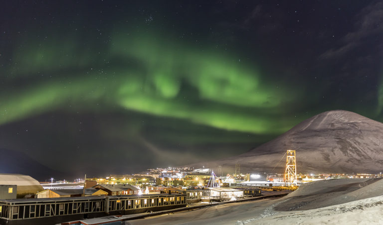 The Northern Lights dancing over Longyearbyen. The tower to the right is part of the old cableway system to the mines © Sophie Cordon