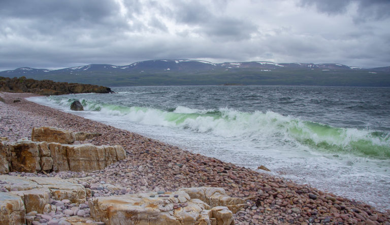 Grønne bølger slår mot den fargerike Luovttat-stranda ved Tanafjorden © Frank Martin Ingilæ
