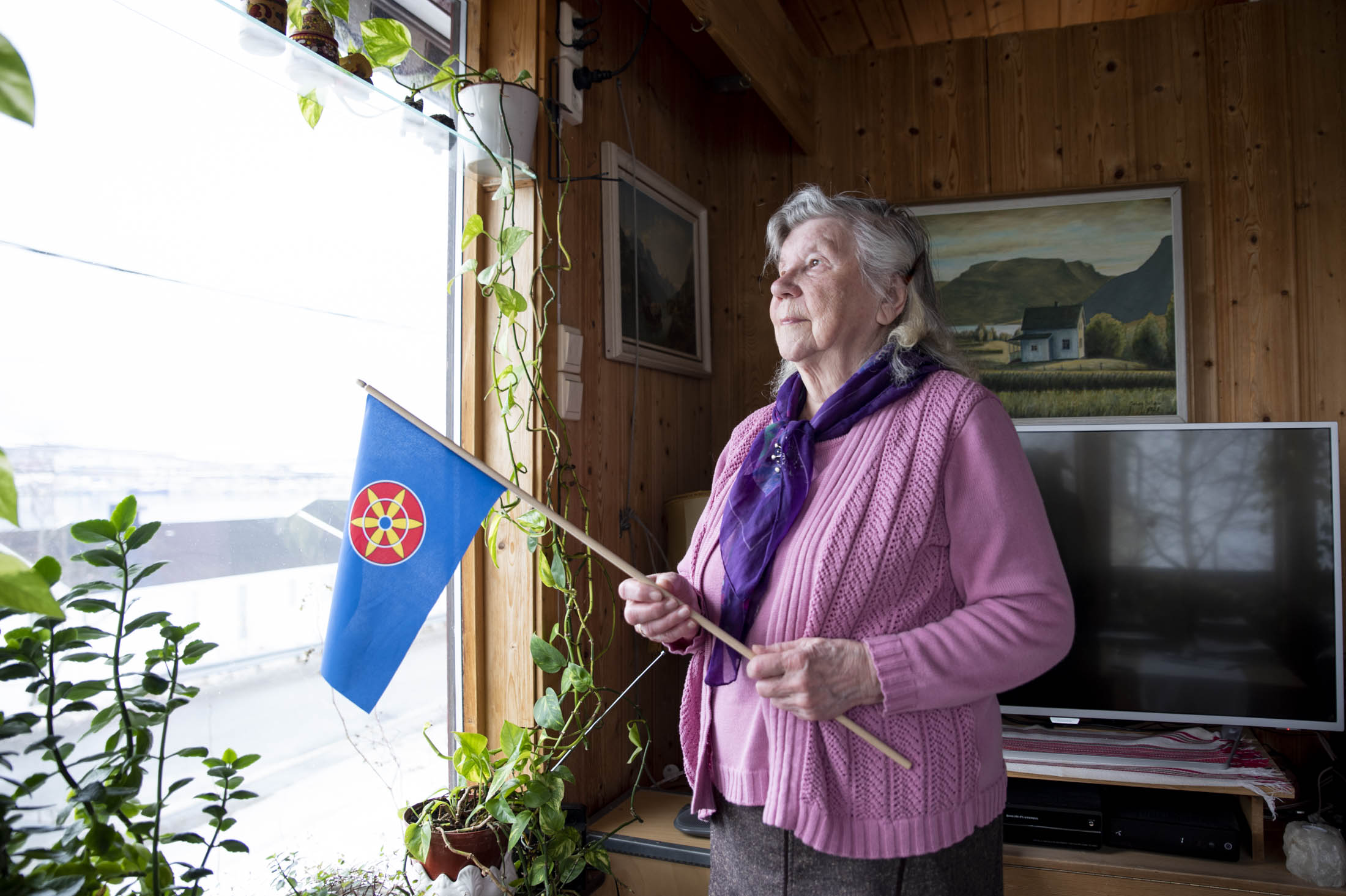 Reidun Mellem holder kvensk flagg og titter ut av vinduet