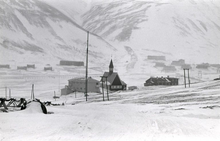 Longyearbyens bebyggelse har flyttet seg rundt i takt med gruvedriften og hvor i dalen gruvene var. Dette bildet er fra ca 1970-1980 og viser Svalbard Kirke og gamle sykehus i forgrunnen. Bak i bildet er det ny bebyggelse i Lia (venstre) samt Haugen med Funktionærmessen (høyre). En vandring i dagens Longyearbyen vil vise deg det samme men med et betydelig større antall bygninger og hus. 

Bildet tilhører © Svalbard museums fotosamling. Fotograf: ukjent. 
